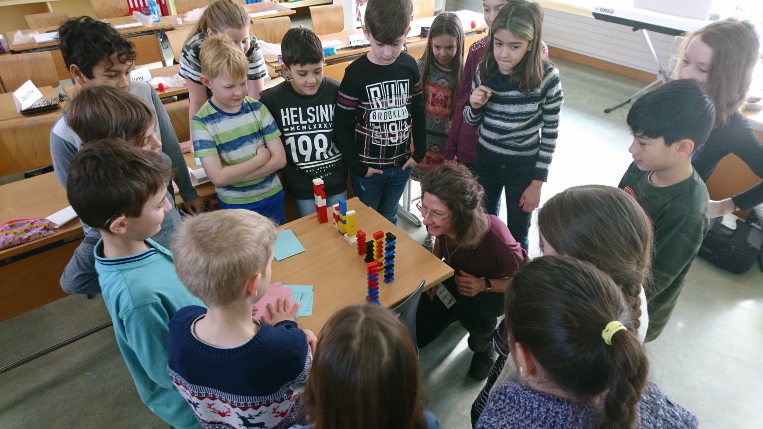 Viele Kinder schauen einer Lehrperson beim konstruieren von Legotürmen zu.